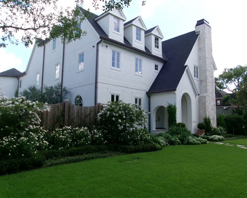 The redesigned front of the home featuring a crisp white stucco finish, updated landscaping with white roses, and a lush green lawn.